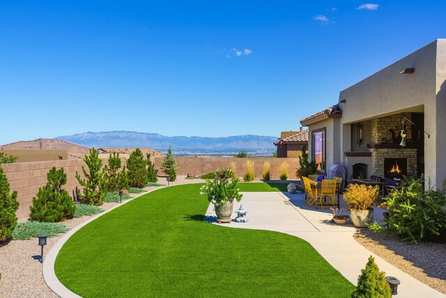 view of yard featuring a mountain view, a patio, and an outdoor stone fireplace