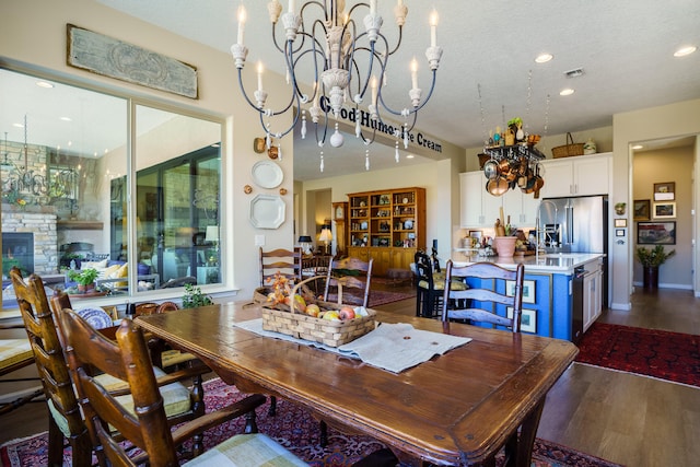 dining area with a chandelier, a textured ceiling, dark hardwood / wood-style flooring, and a stone fireplace