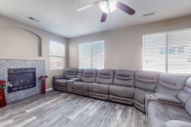 living room featuring a tiled fireplace, ceiling fan, a textured ceiling, and hardwood / wood-style flooring