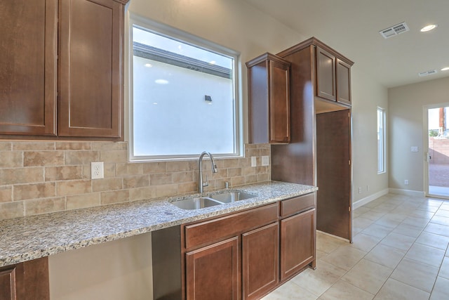 kitchen with light stone countertops, light tile patterned floors, tasteful backsplash, and sink