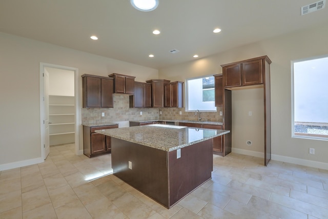 kitchen featuring a kitchen island, light stone countertops, backsplash, and a wealth of natural light