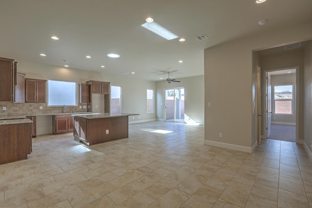 kitchen with ceiling fan, sink, light stone counters, backsplash, and a kitchen island