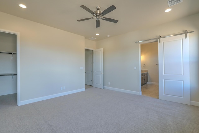 unfurnished bedroom with a spacious closet, ceiling fan, a barn door, light colored carpet, and a closet