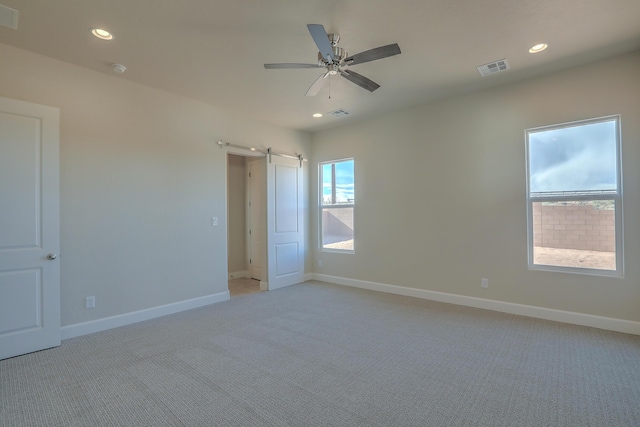 unfurnished room with light carpet, a barn door, and ceiling fan