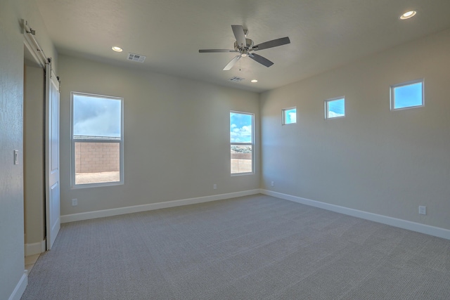 carpeted spare room with ceiling fan and a barn door