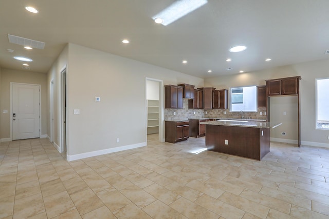 kitchen with backsplash, a kitchen island, a healthy amount of sunlight, and light stone counters