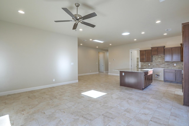 kitchen with a kitchen island with sink, ceiling fan, decorative backsplash, light stone countertops, and light tile patterned floors