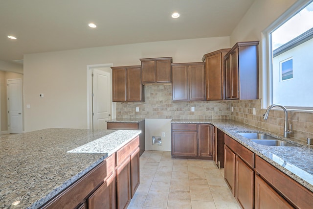 kitchen featuring light stone countertops, backsplash, light tile patterned flooring, and sink