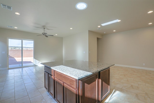 kitchen featuring light stone countertops, a kitchen island, light tile patterned floors, and ceiling fan