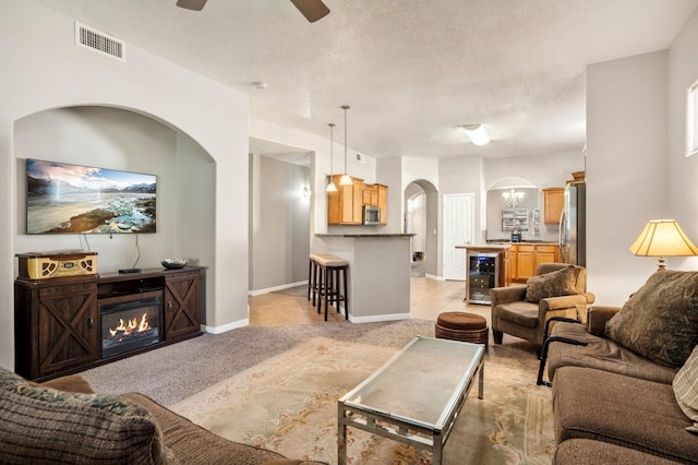 living room featuring a textured ceiling, wine cooler, light carpet, and ceiling fan with notable chandelier