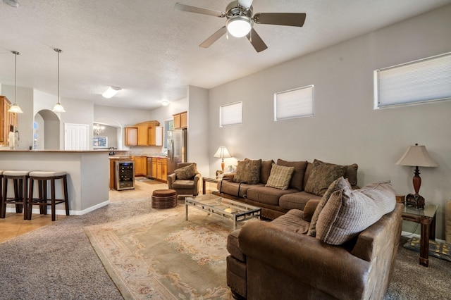 living area with a ceiling fan, beverage cooler, arched walkways, a textured ceiling, and light carpet