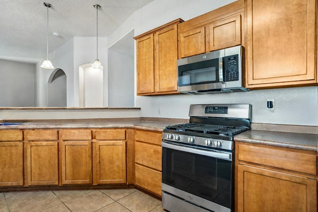 kitchen with a textured ceiling, light tile patterned floors, hanging light fixtures, and appliances with stainless steel finishes