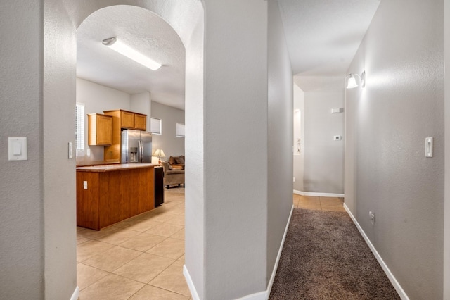 hall with baseboards, light tile patterned floors, a textured wall, arched walkways, and a textured ceiling