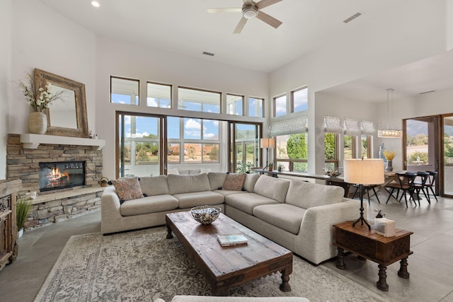 living room featuring ceiling fan with notable chandelier, a fireplace, a high ceiling, and concrete floors