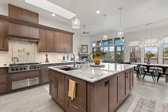 kitchen featuring stainless steel gas stovetop, sink, ceiling fan, an island with sink, and tasteful backsplash