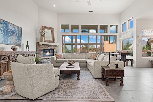 living room featuring ceiling fan, a stone fireplace, and a high ceiling