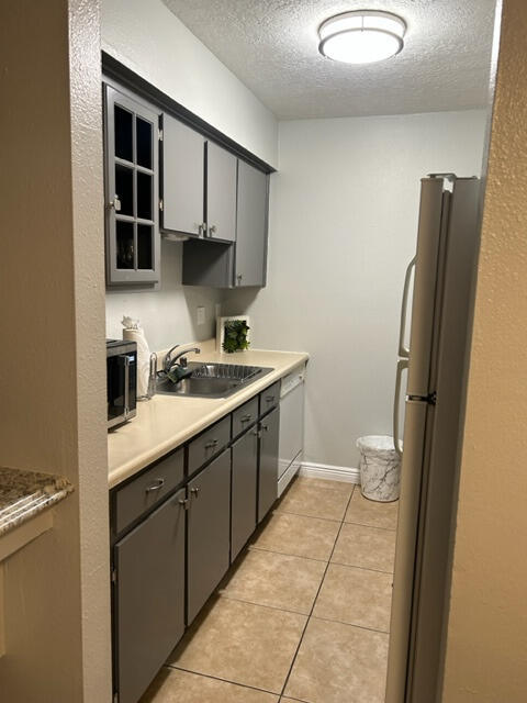 kitchen with light tile patterned flooring, stainless steel appliances, a textured ceiling, gray cabinets, and sink