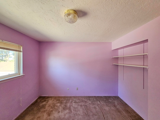 unfurnished room featuring dark colored carpet and a textured ceiling