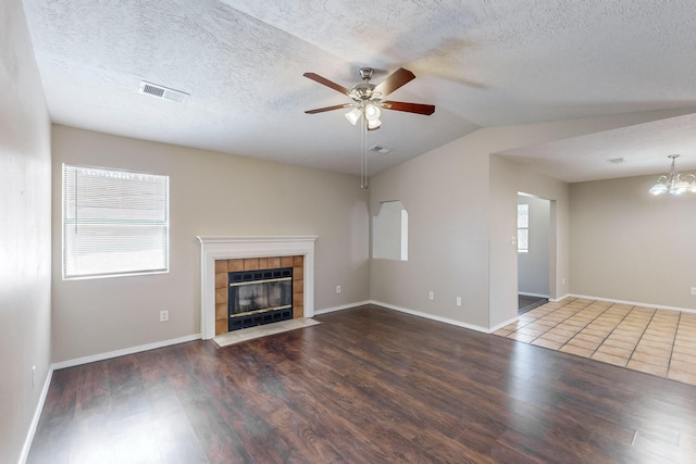 unfurnished living room featuring ceiling fan with notable chandelier, a textured ceiling, a fireplace, dark wood-type flooring, and vaulted ceiling