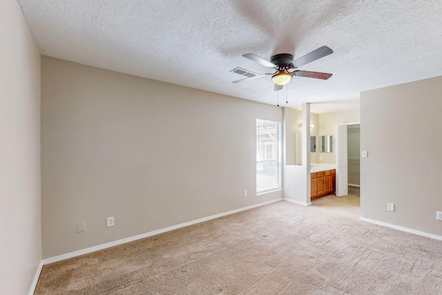 unfurnished bedroom with ensuite bathroom, a textured ceiling, light carpet, and ceiling fan