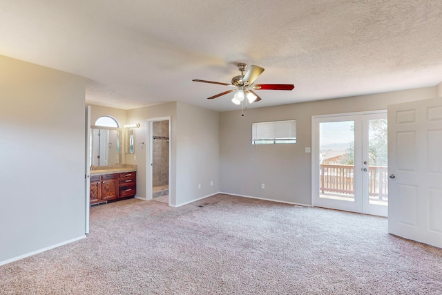 unfurnished bedroom featuring ensuite bath, light colored carpet, access to exterior, a textured ceiling, and ceiling fan