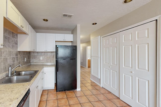 kitchen featuring backsplash, light tile patterned floors, black refrigerator, sink, and white cabinets