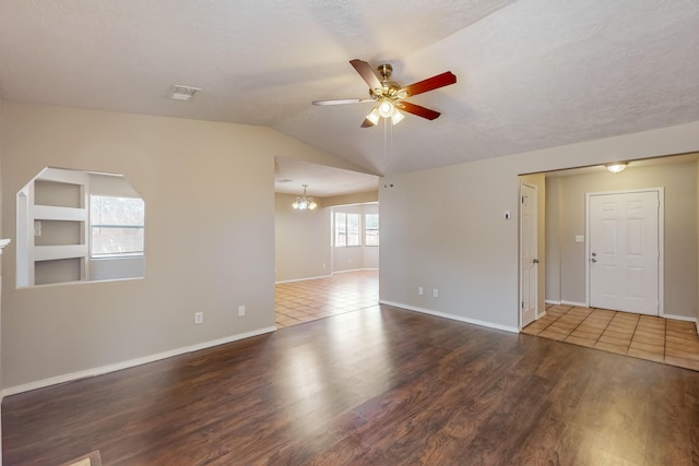 spare room featuring vaulted ceiling, ceiling fan with notable chandelier, a healthy amount of sunlight, and dark hardwood / wood-style flooring