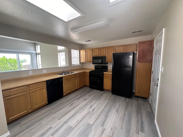 kitchen with black appliances, a skylight, sink, and light hardwood / wood-style flooring