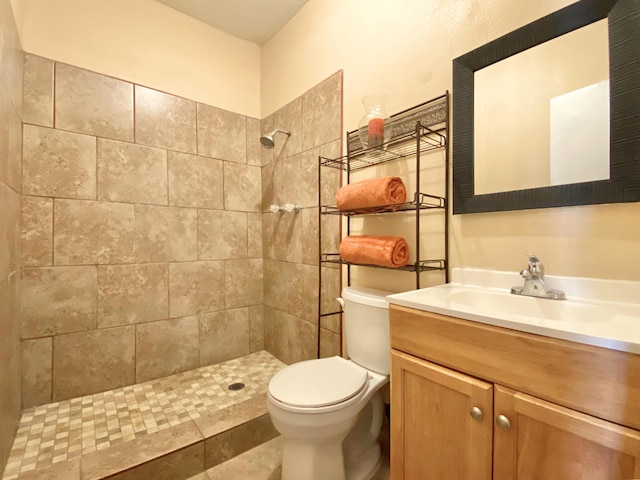 bathroom with a tile shower, vanity, and toilet