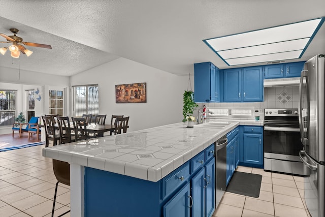 kitchen featuring blue cabinetry, tile counters, sink, stainless steel appliances, and lofted ceiling