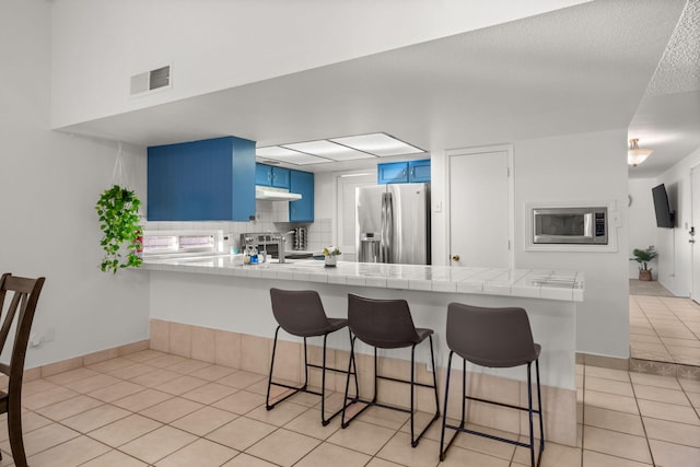 kitchen featuring kitchen peninsula, a breakfast bar, stainless steel appliances, blue cabinetry, and light tile patterned floors