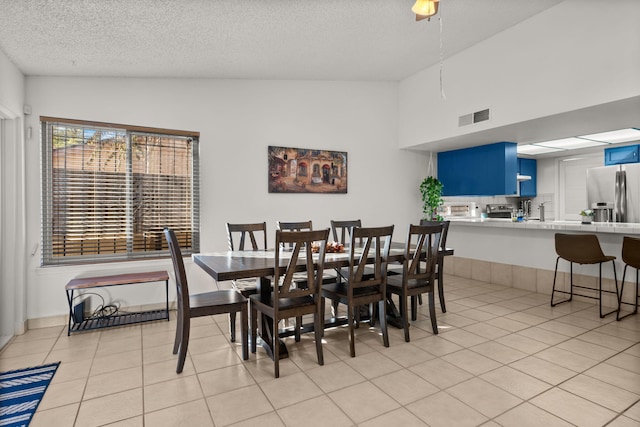 dining room with a textured ceiling, high vaulted ceiling, and light tile patterned flooring