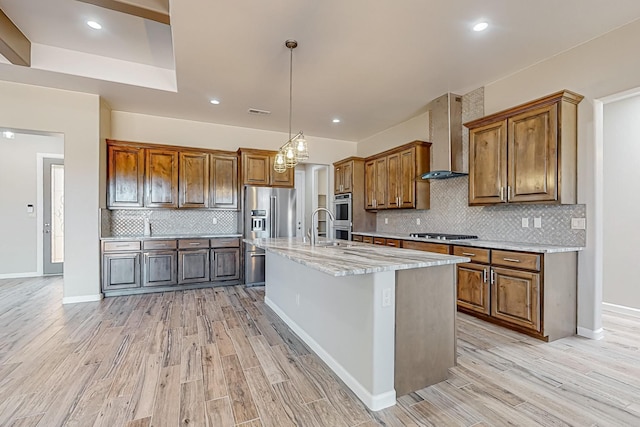 kitchen featuring decorative backsplash, wall chimney exhaust hood, a center island with sink, and light hardwood / wood-style floors