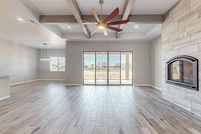 unfurnished living room with light wood-type flooring, a tile fireplace, ceiling fan, and beamed ceiling