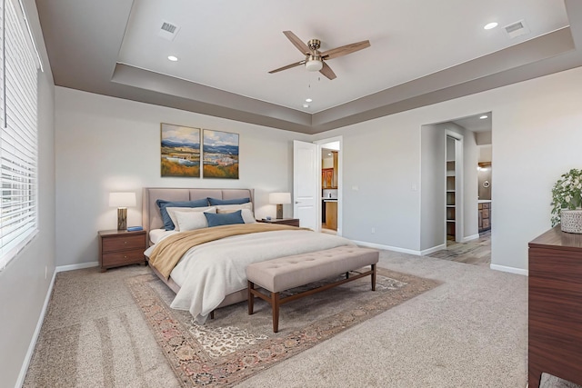 bedroom featuring light carpet, ceiling fan, and a tray ceiling