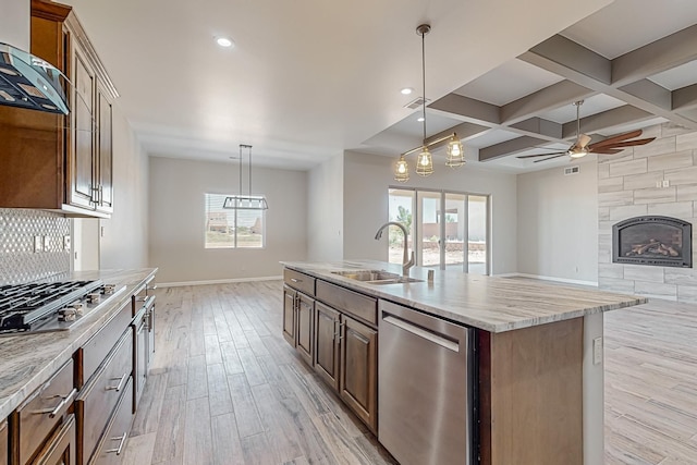 kitchen with a center island with sink, sink, appliances with stainless steel finishes, wall chimney exhaust hood, and coffered ceiling