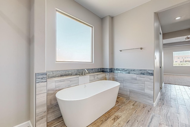 bathroom featuring a bathtub, tile walls, hardwood / wood-style floors, and ceiling fan