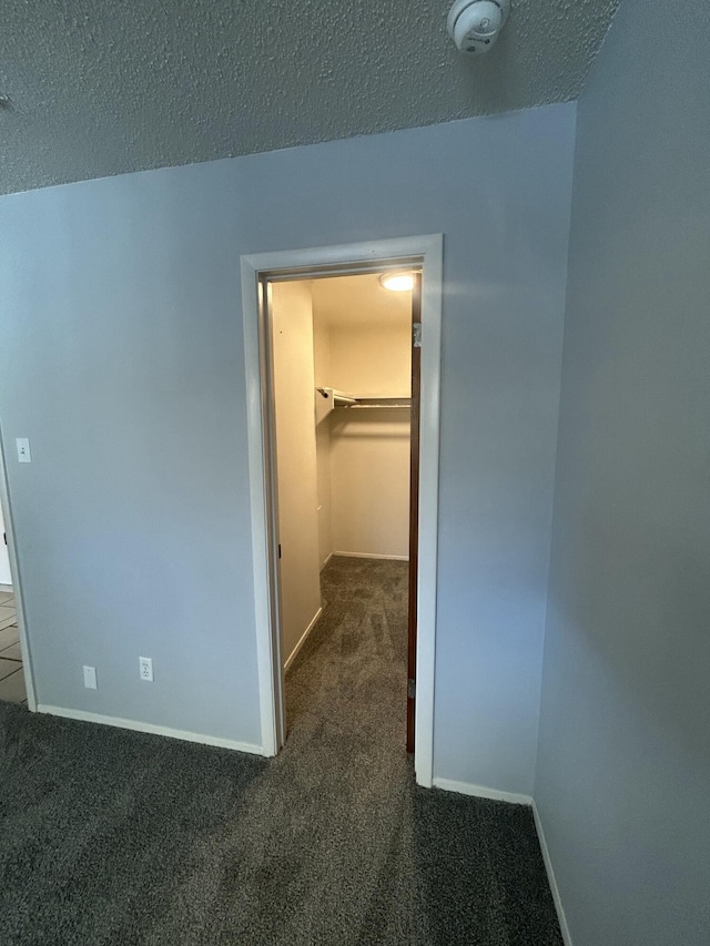 corridor featuring a textured ceiling and dark carpet