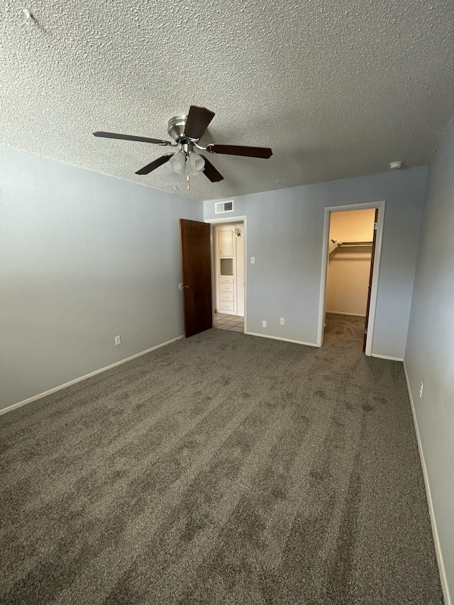 unfurnished bedroom featuring a textured ceiling, ceiling fan, dark colored carpet, a spacious closet, and a closet