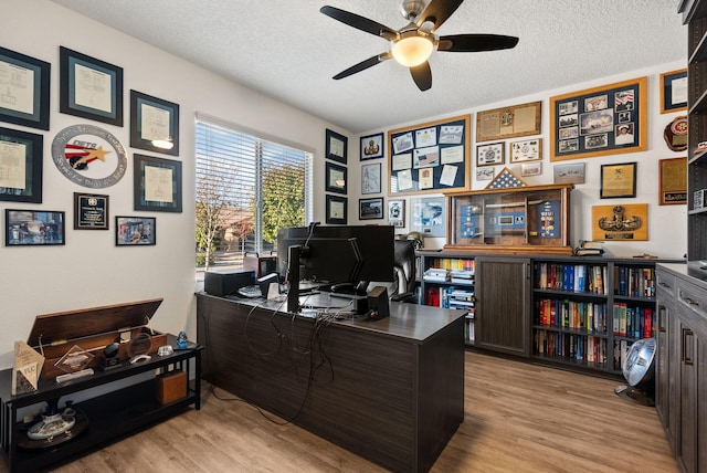 home office with light hardwood / wood-style floors, ceiling fan, and a textured ceiling