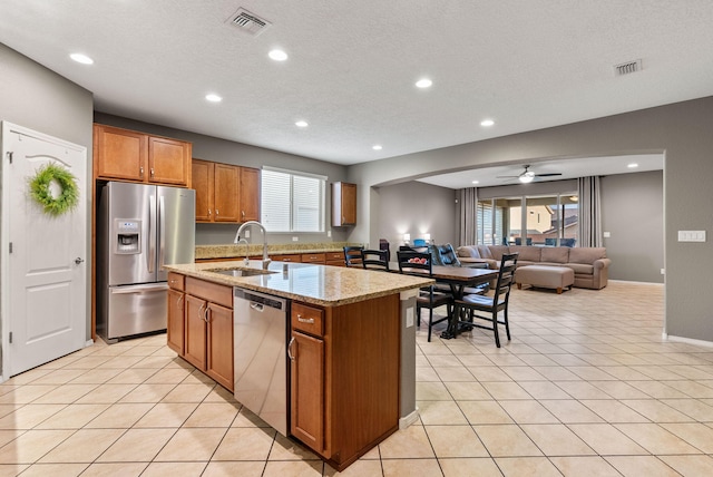 kitchen with stainless steel appliances, light stone counters, sink, light tile patterned floors, and an island with sink