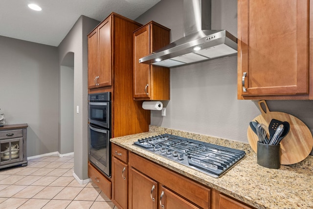 kitchen featuring light stone counters, wall chimney range hood, stainless steel gas cooktop, and light tile patterned floors