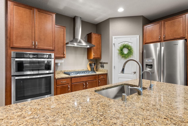 kitchen featuring appliances with stainless steel finishes, sink, wall chimney range hood, and light stone countertops