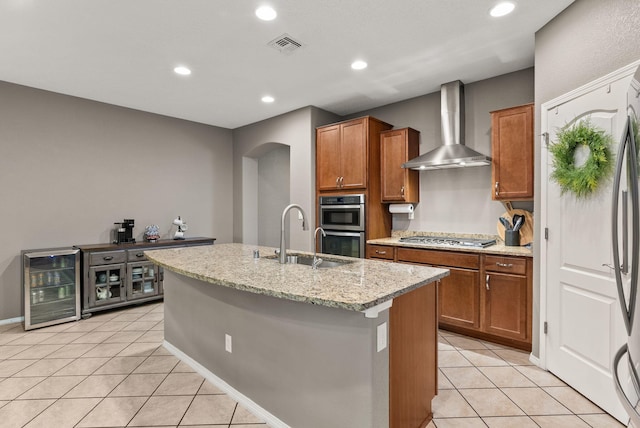 kitchen featuring stainless steel appliances, a center island with sink, beverage cooler, light tile patterned flooring, and wall chimney range hood