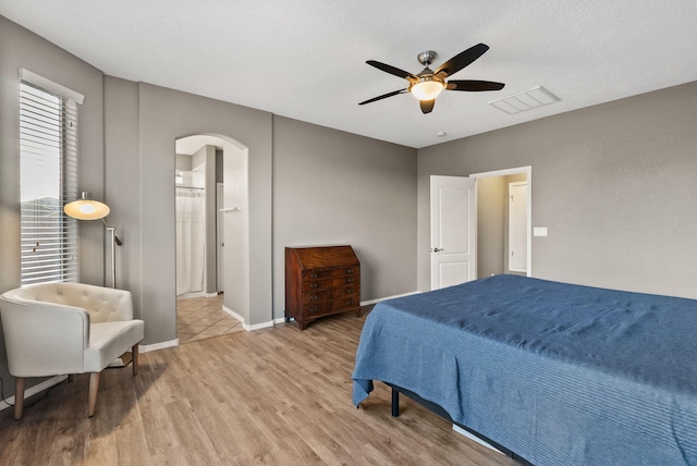 bedroom with light hardwood / wood-style floors, ceiling fan, connected bathroom, and a textured ceiling