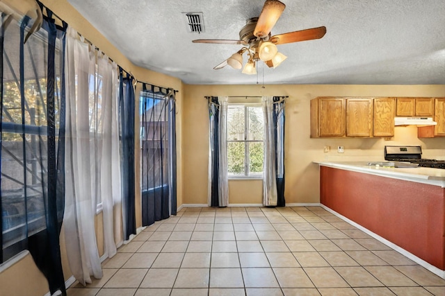 kitchen with a textured ceiling, gas range, light tile patterned floors, and ceiling fan