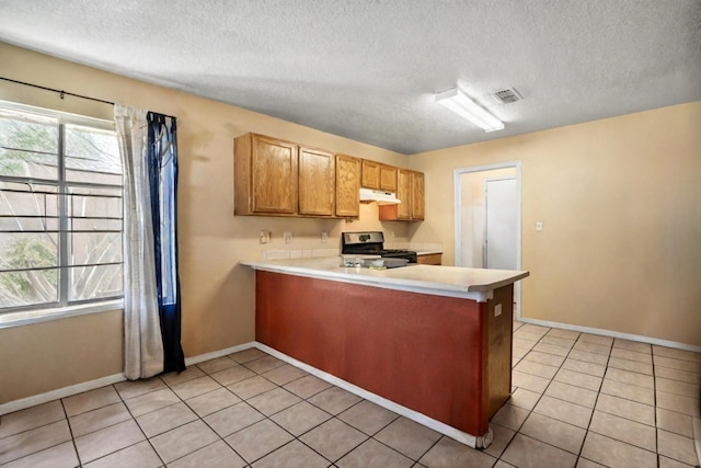 kitchen with stainless steel gas range, a textured ceiling, light tile patterned floors, and kitchen peninsula