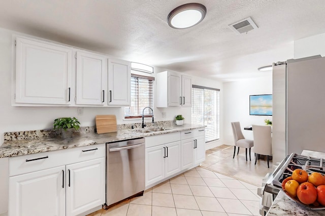 kitchen with white cabinets, sink, stainless steel dishwasher, a textured ceiling, and light tile patterned flooring