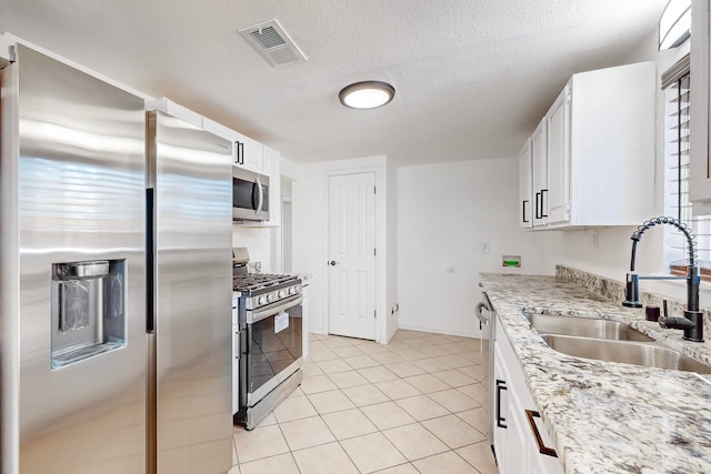 kitchen with white cabinets, sink, light stone countertops, a textured ceiling, and appliances with stainless steel finishes