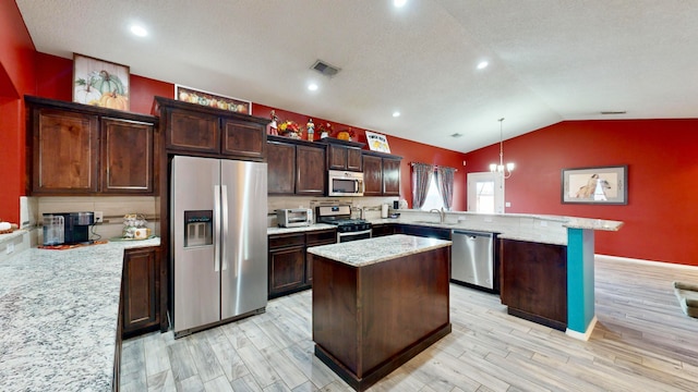 kitchen with a kitchen island, appliances with stainless steel finishes, decorative light fixtures, and lofted ceiling